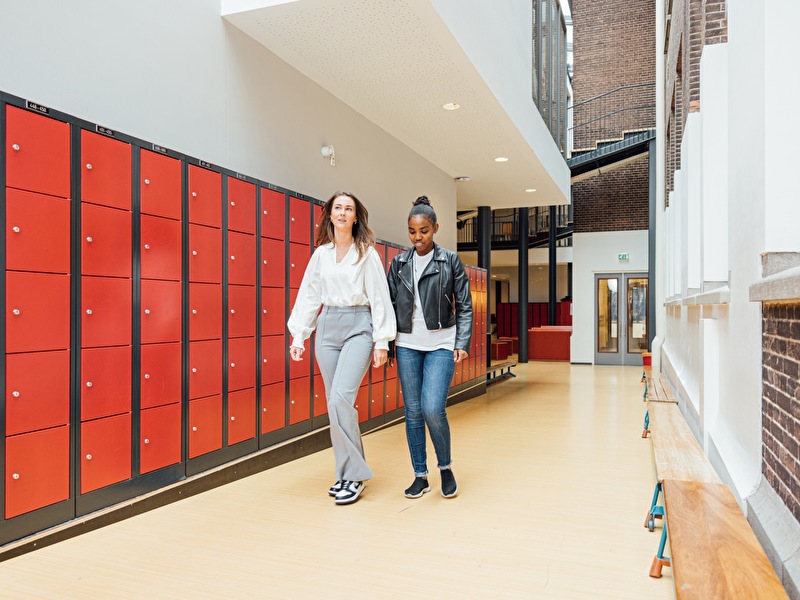 Jeugdverpleegkundige en leerling maken een praatje in de gang van een middelbare school